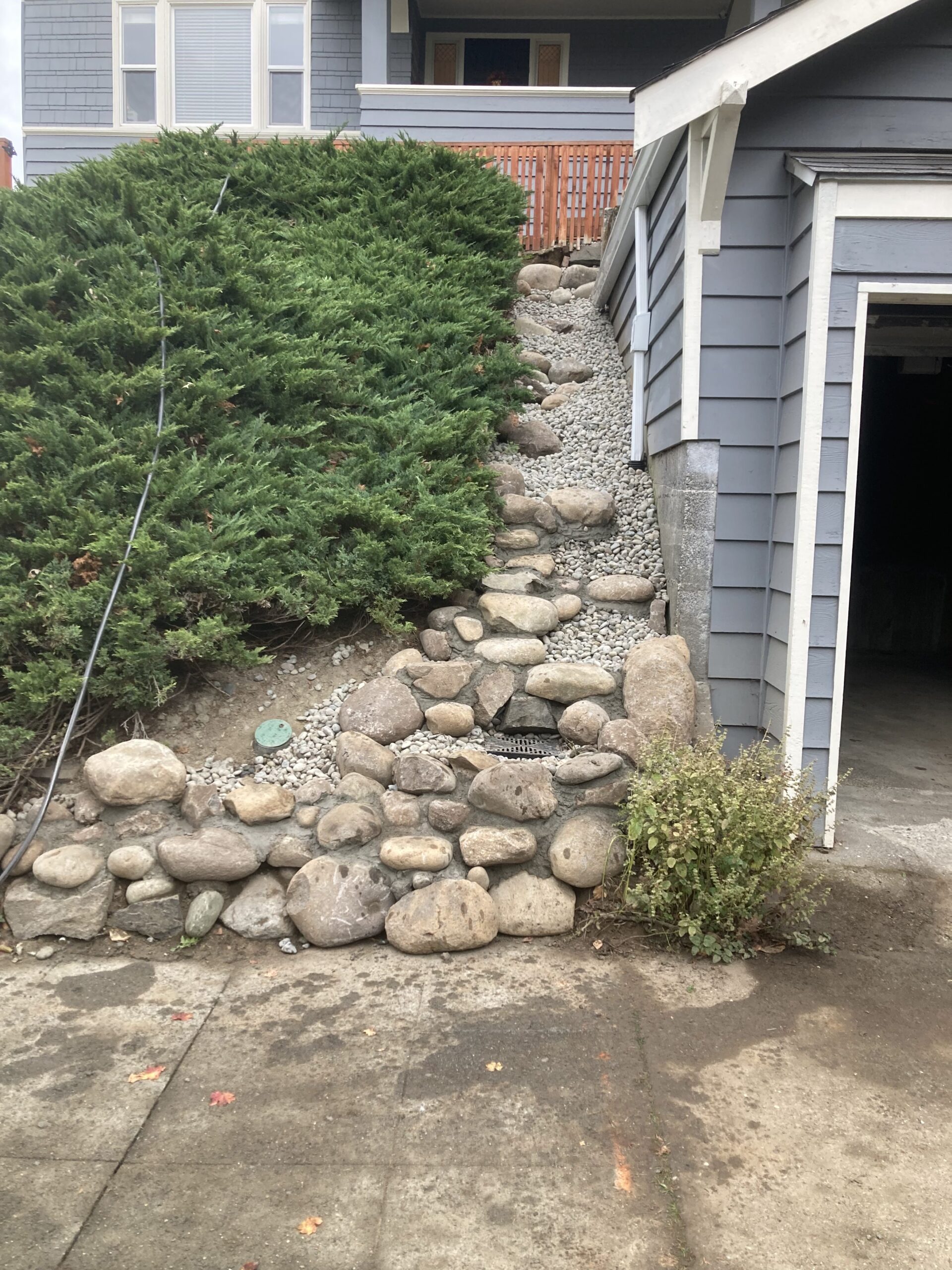 a narrow, sloped, stone retaining wall and drainage area by a house